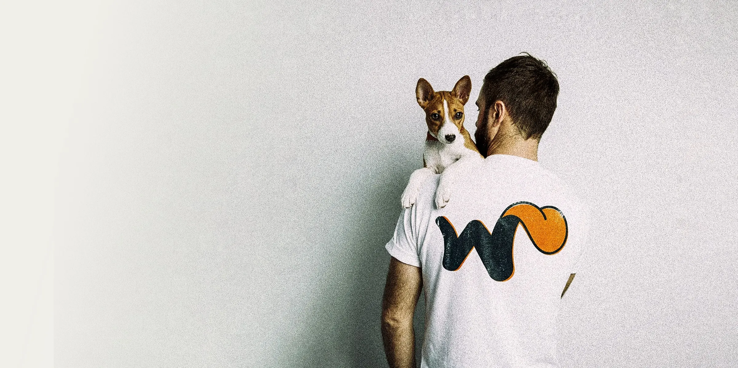Tutor de espaldas con remera de Wana sosteniendo a un cachorro sobre el hombro
